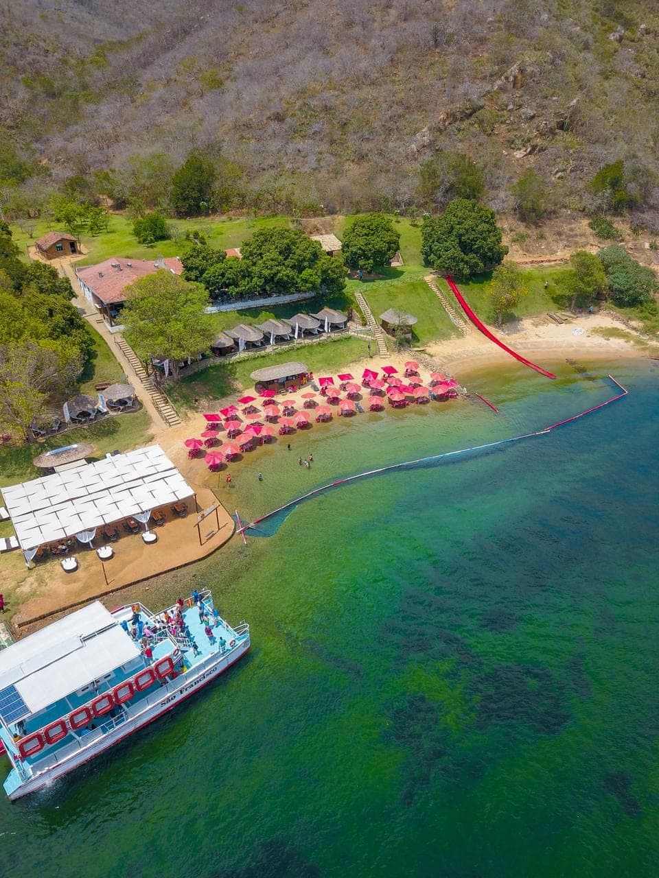 Prainha do Angico vista do alto, com guarda-sóis na areia e embarcação atracada